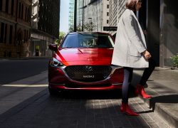 Mazda2 bei Auto Stahl Modellabbildung in der Modellfarbe rot in Frontansicht mit vorbeigehender Frau